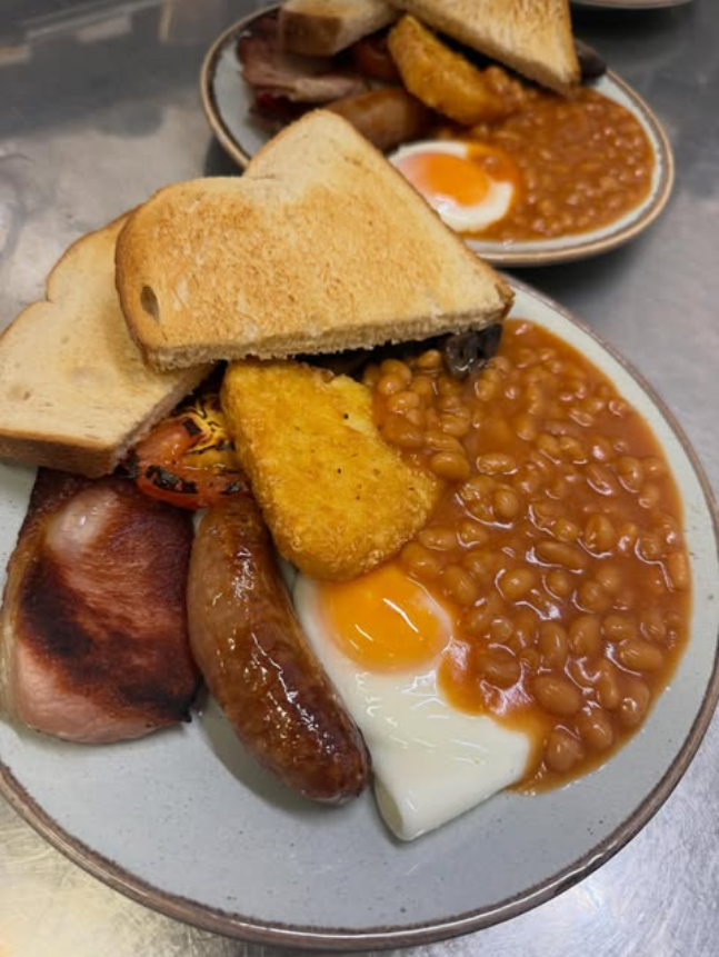 A cooked English breakfast with toast, a hash brown, sausages and beans