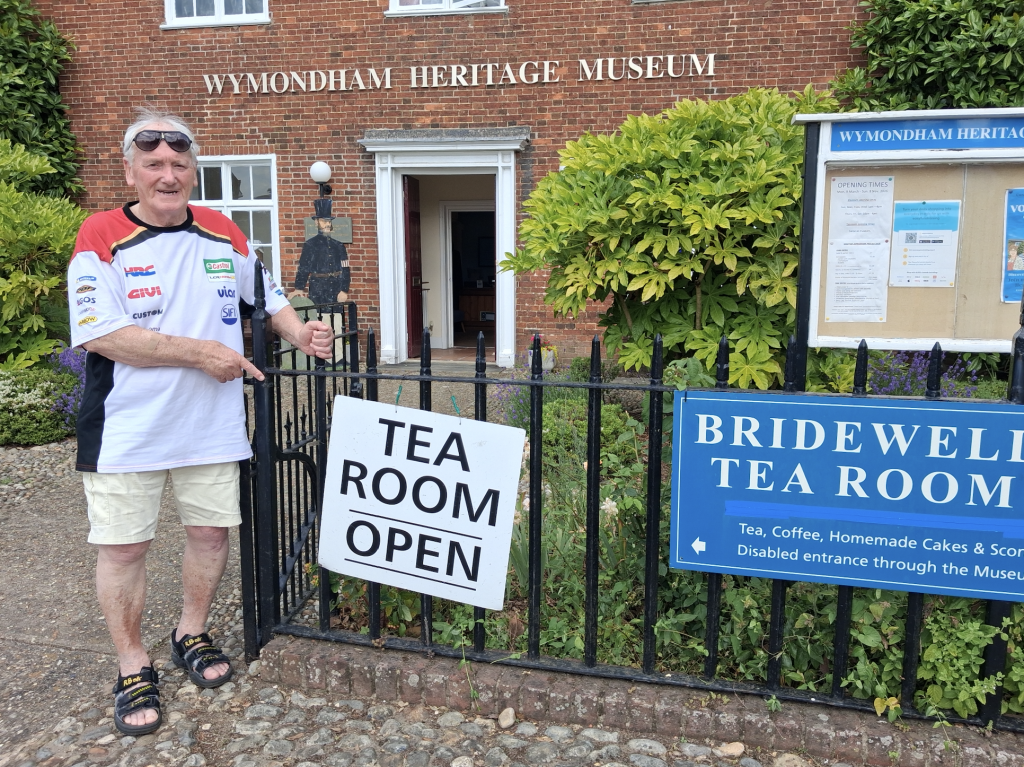 Man standing in front of a sign saying 'Tea Room Open'