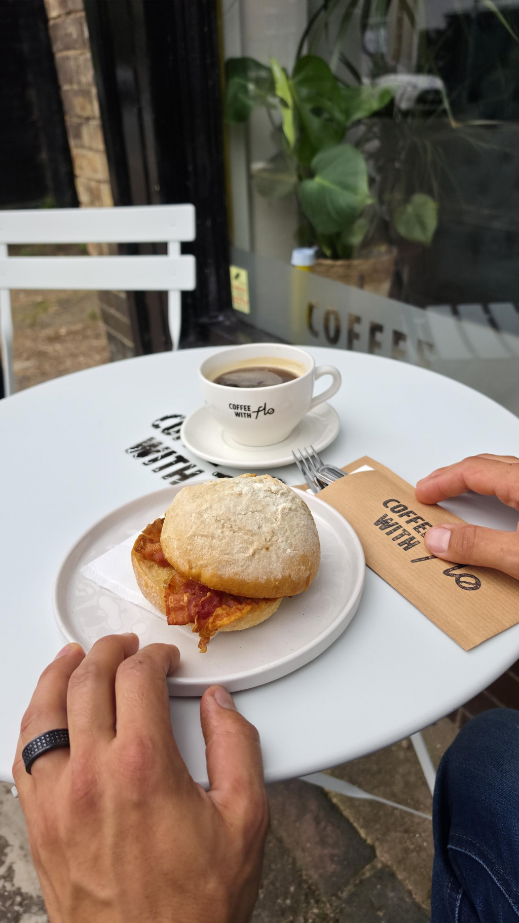 Bacon bap on a plate with a cup of coffee