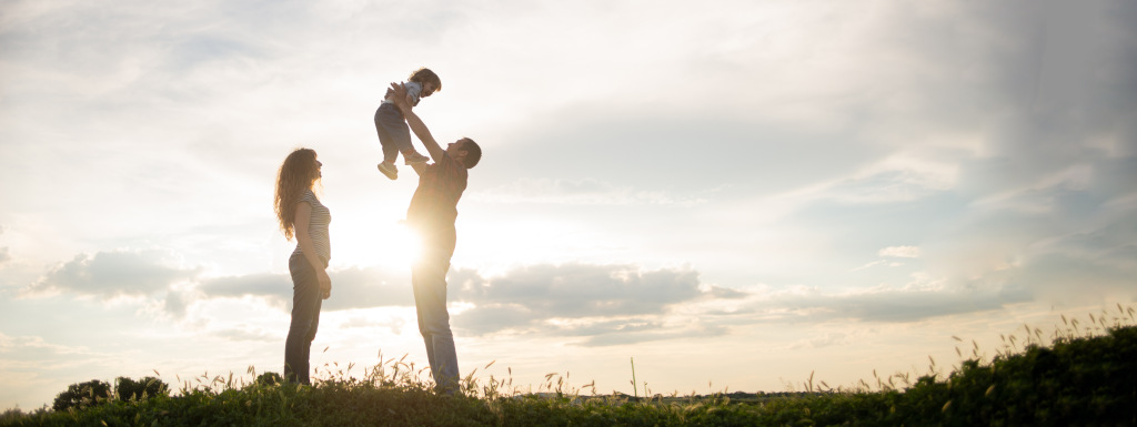 A man, woman and their young daughter silhouetted against a sunset sky