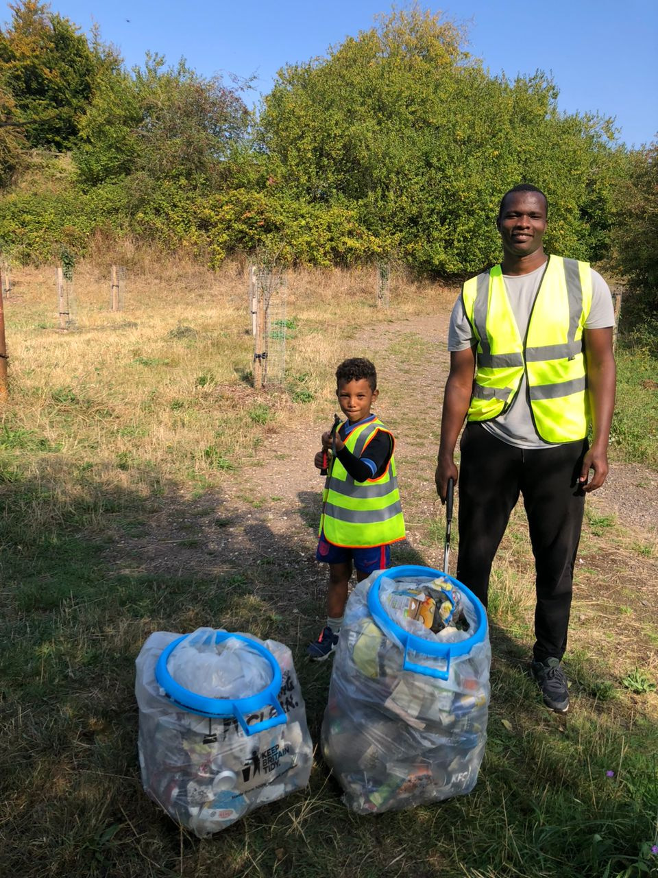 Father and son in high-vis jackets with bags of rubbish