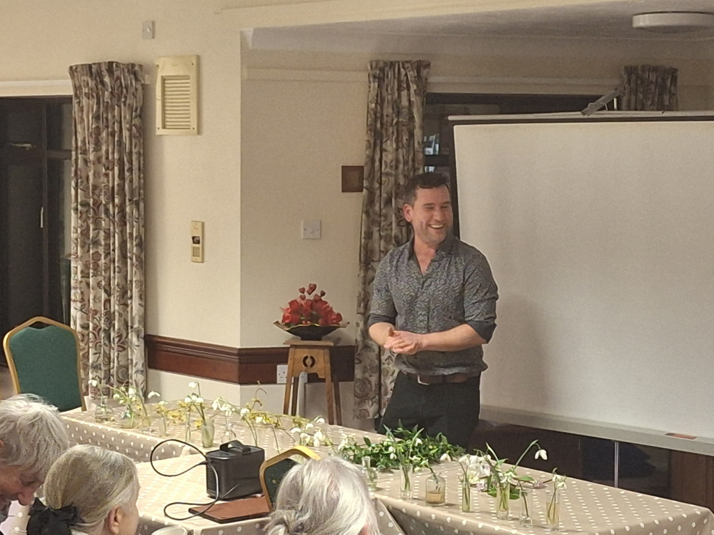 Man standing in front of a white board with a desk of plants in front of him