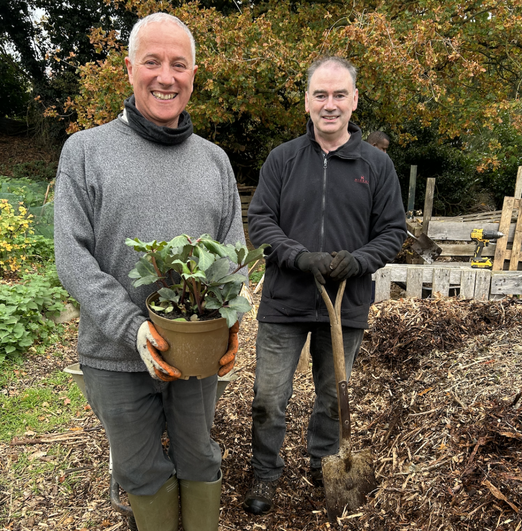 Two people smiling, one holding a potted plant