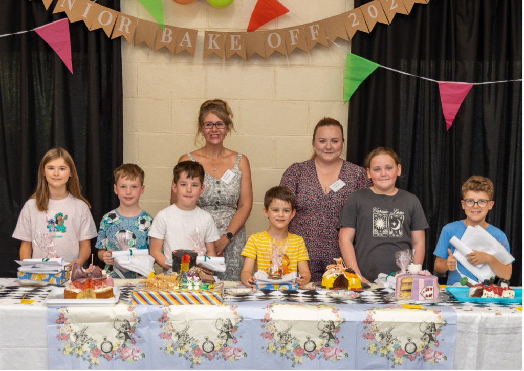 Two women standing behind a row of child bakers with their cakes on a table