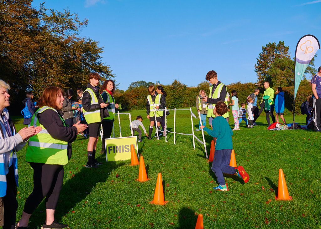 Spectators in high-vis jackets cheering as a child runs down a path of orange cones