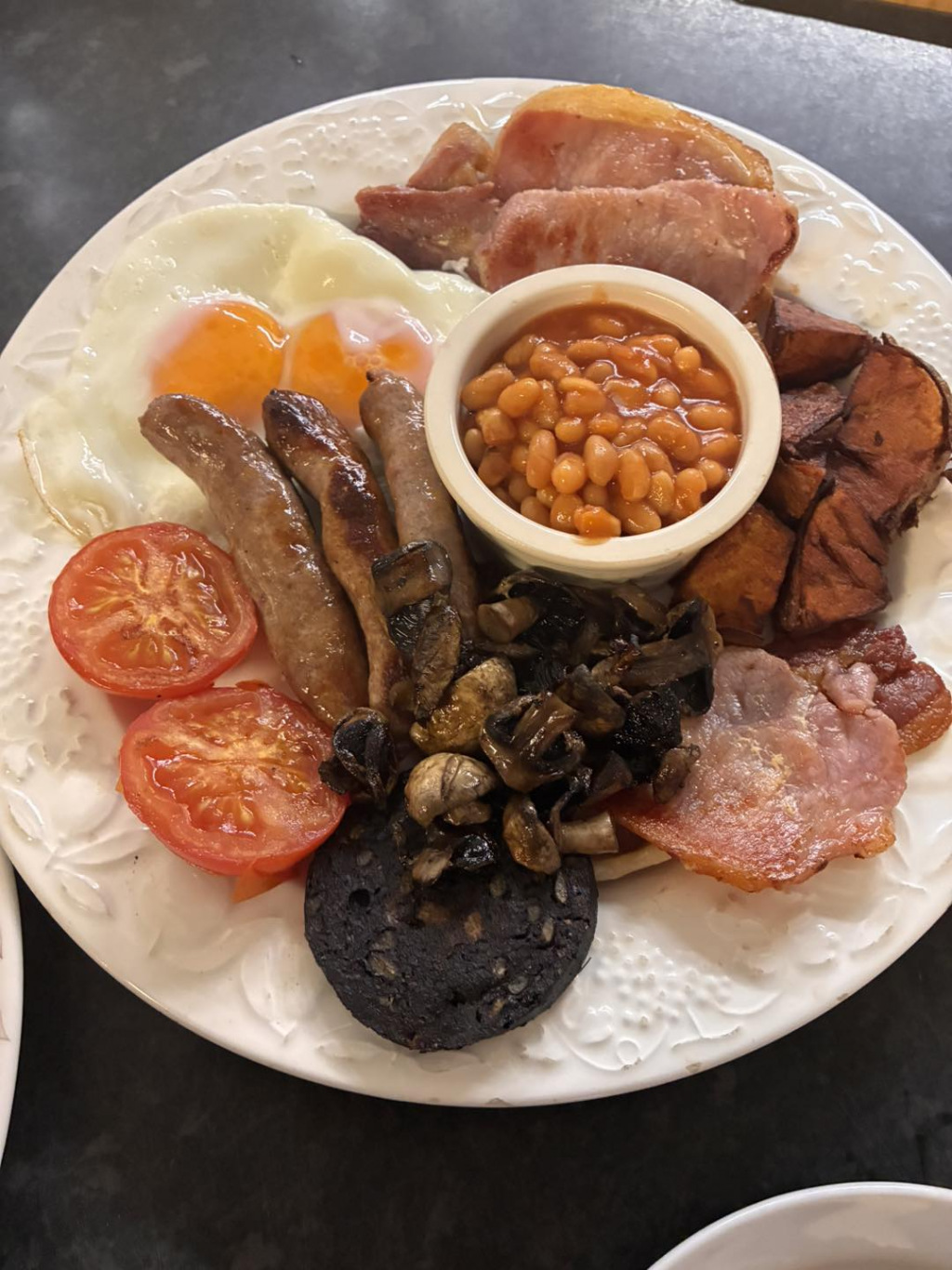 A plate of sausages, mushrooms, tomatoes, and a ceramic pot of baked beans