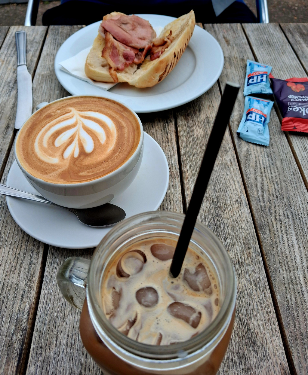 An iced tea, a coffee, and an open bacon sarnie on a table