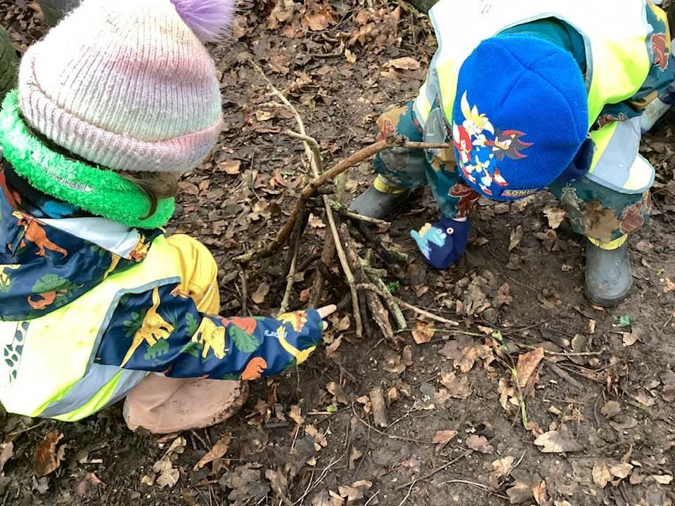 Two children in raincoats and hats investigating the soil with their backs to the camera