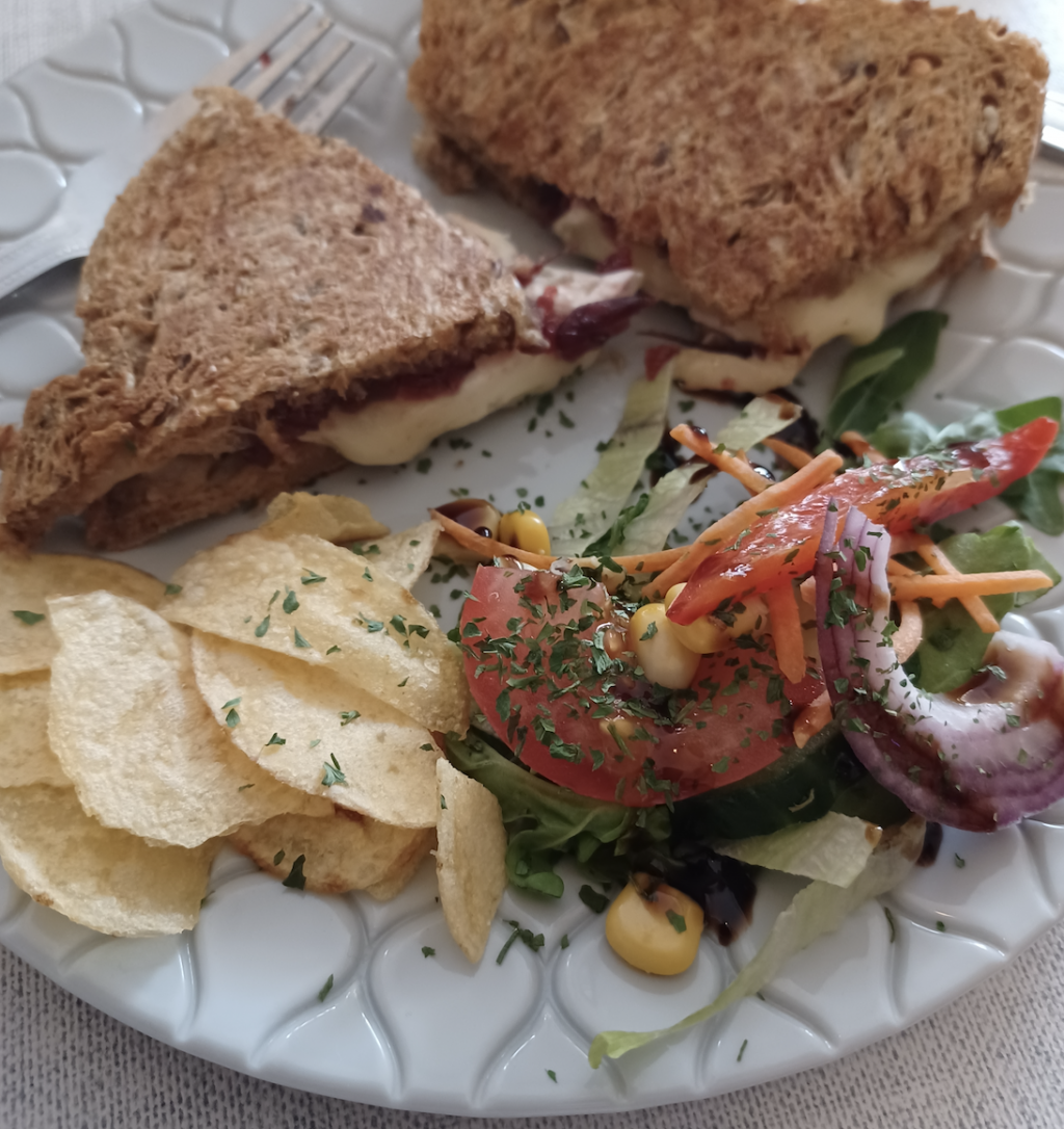 A sandwich on a plate with crisps and salad