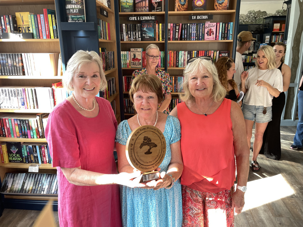 Three women smiling with wooden trophy