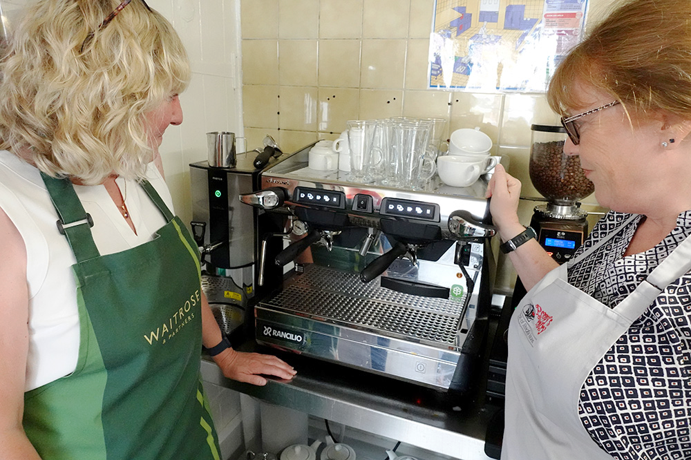 Two kitchen workers stood in front of a coffee machine