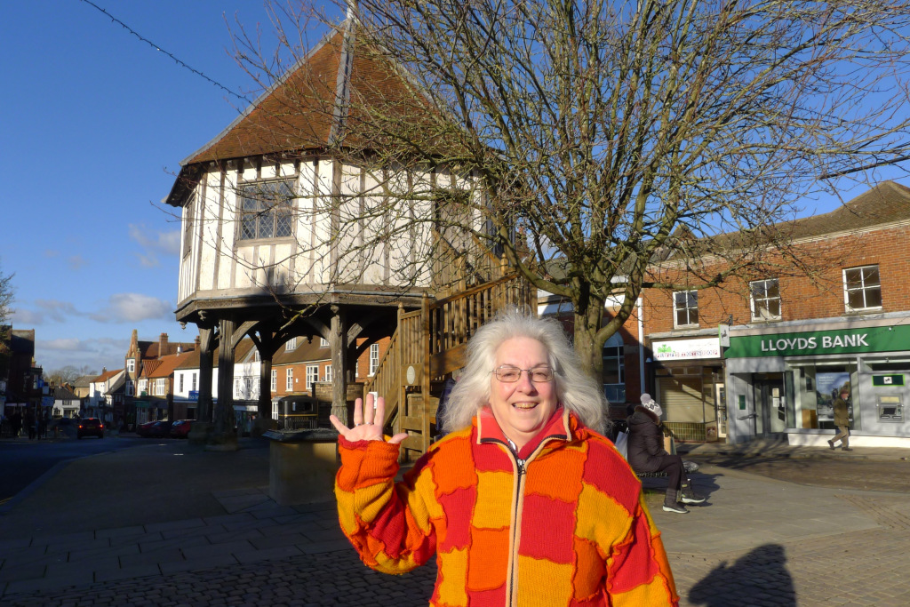 Lady in bright jumper waves with market cross in background