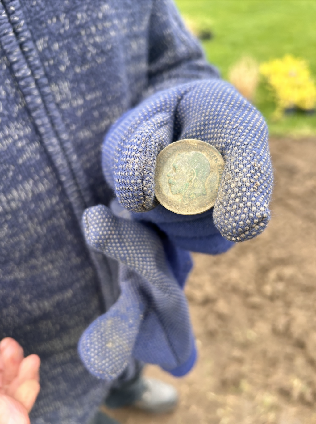 A gloved hand holding an old coin