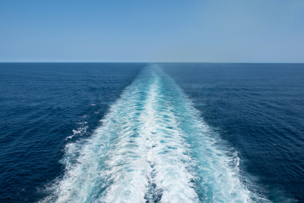 A shot of the dark blue sea with a white, bubbly boat trail running down the centre
