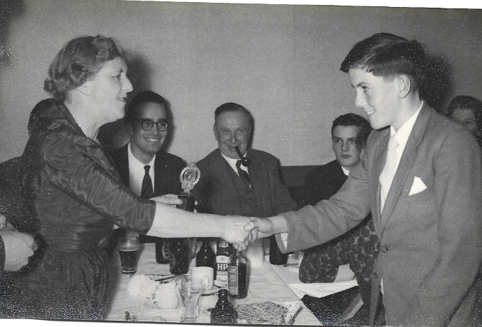 Black-and-white still of a young man shaking hands with a woman