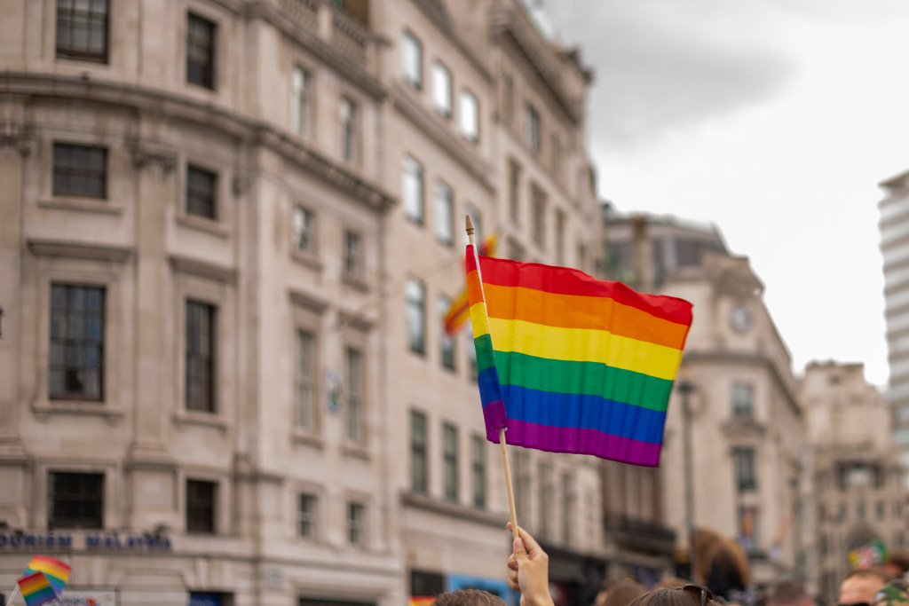 A hand waving a Pride rainbow flag outside a building