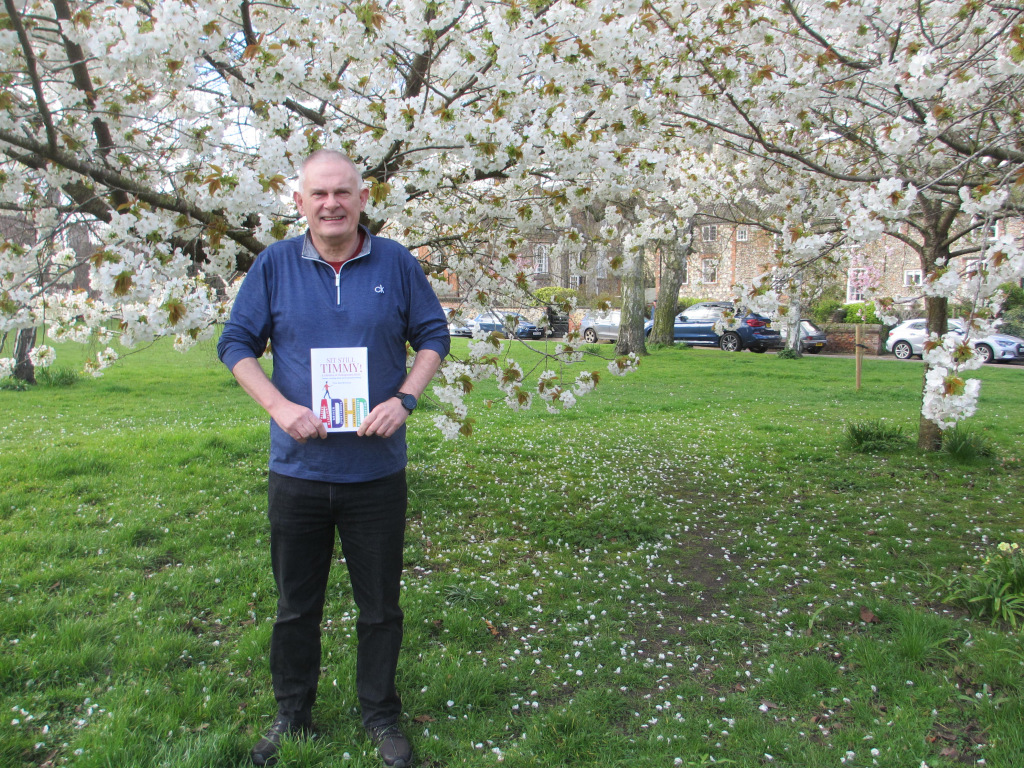 Man holds book standing in front of tree with white flowers