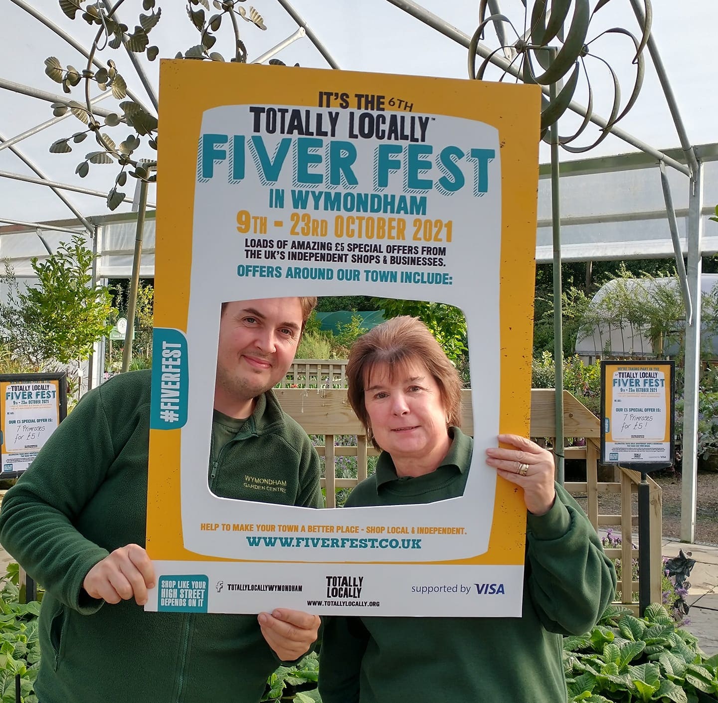 Garden centre employees pose in Totally Locally cardboard frame