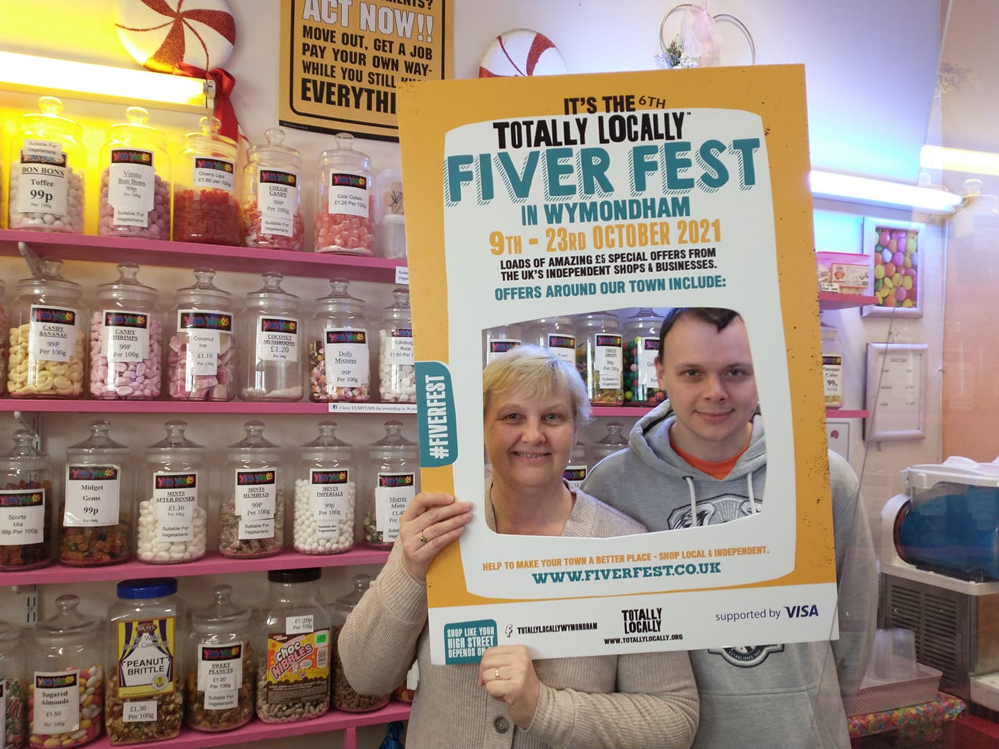 Two shopkeepers pose in Totally Locally cardboard frame