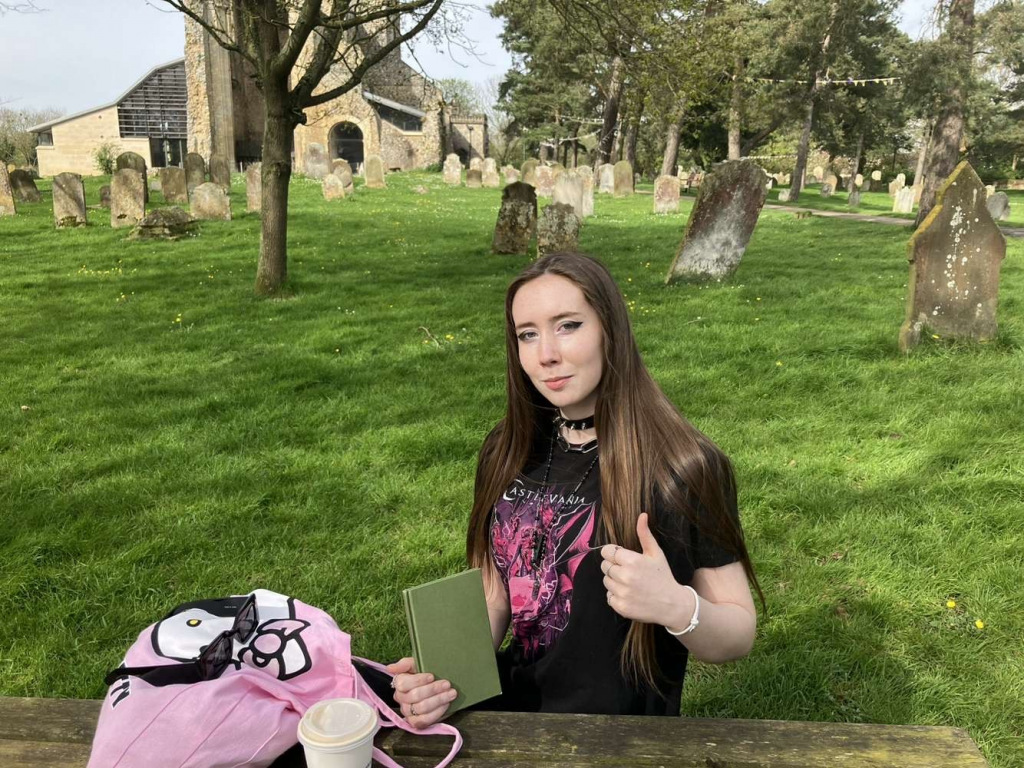 Girl holding book with thumb up sitting outside in churchyard