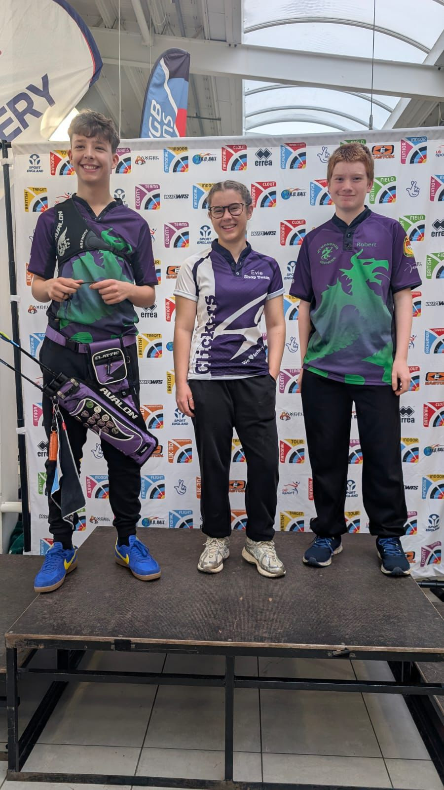 Three people on a podium wearing archery medals